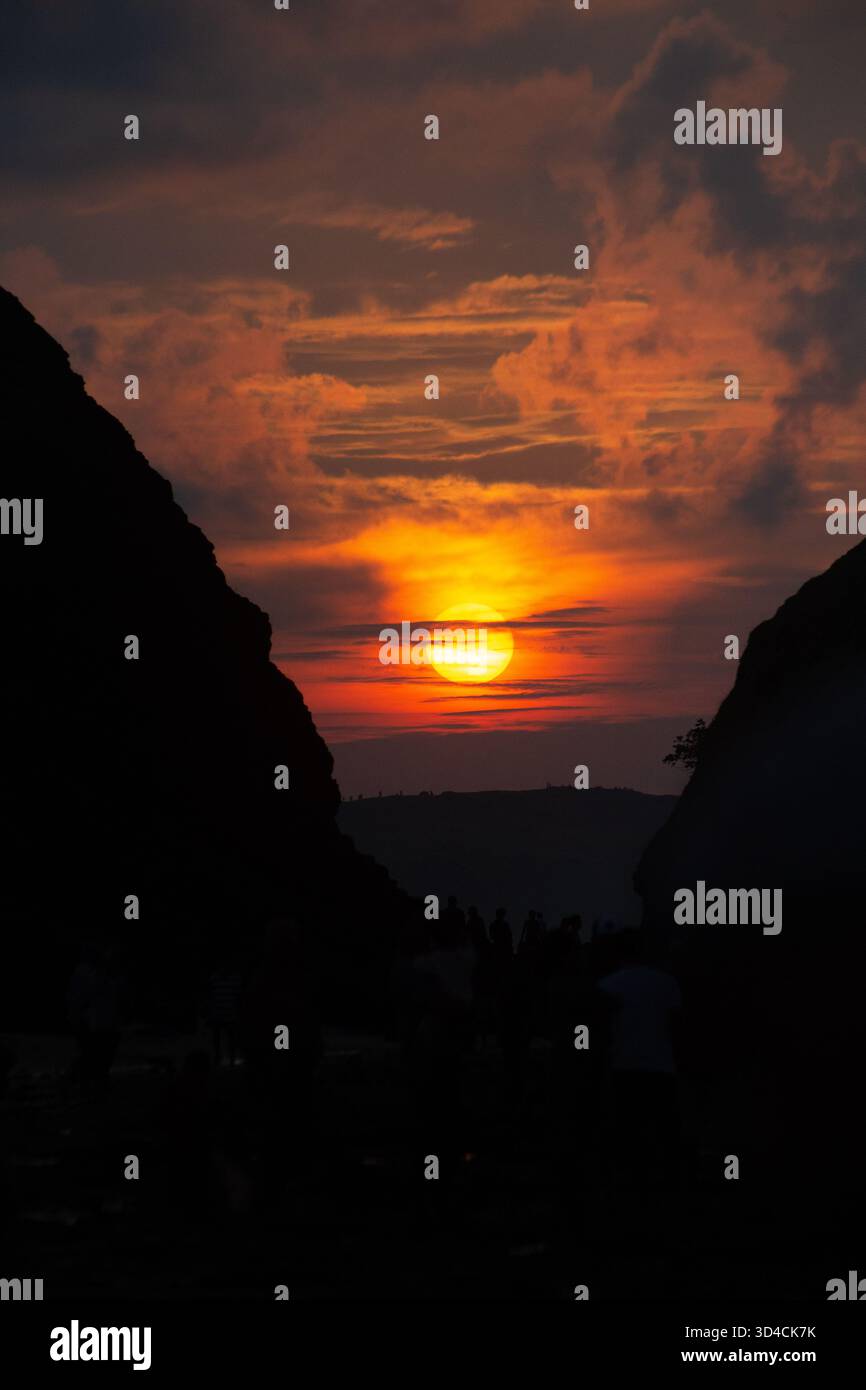 A stunning sunset view between cliffs at Seger Beach, Central Lombok, Indonesia. The sun glows brightly through layers of clouds Stock Photo