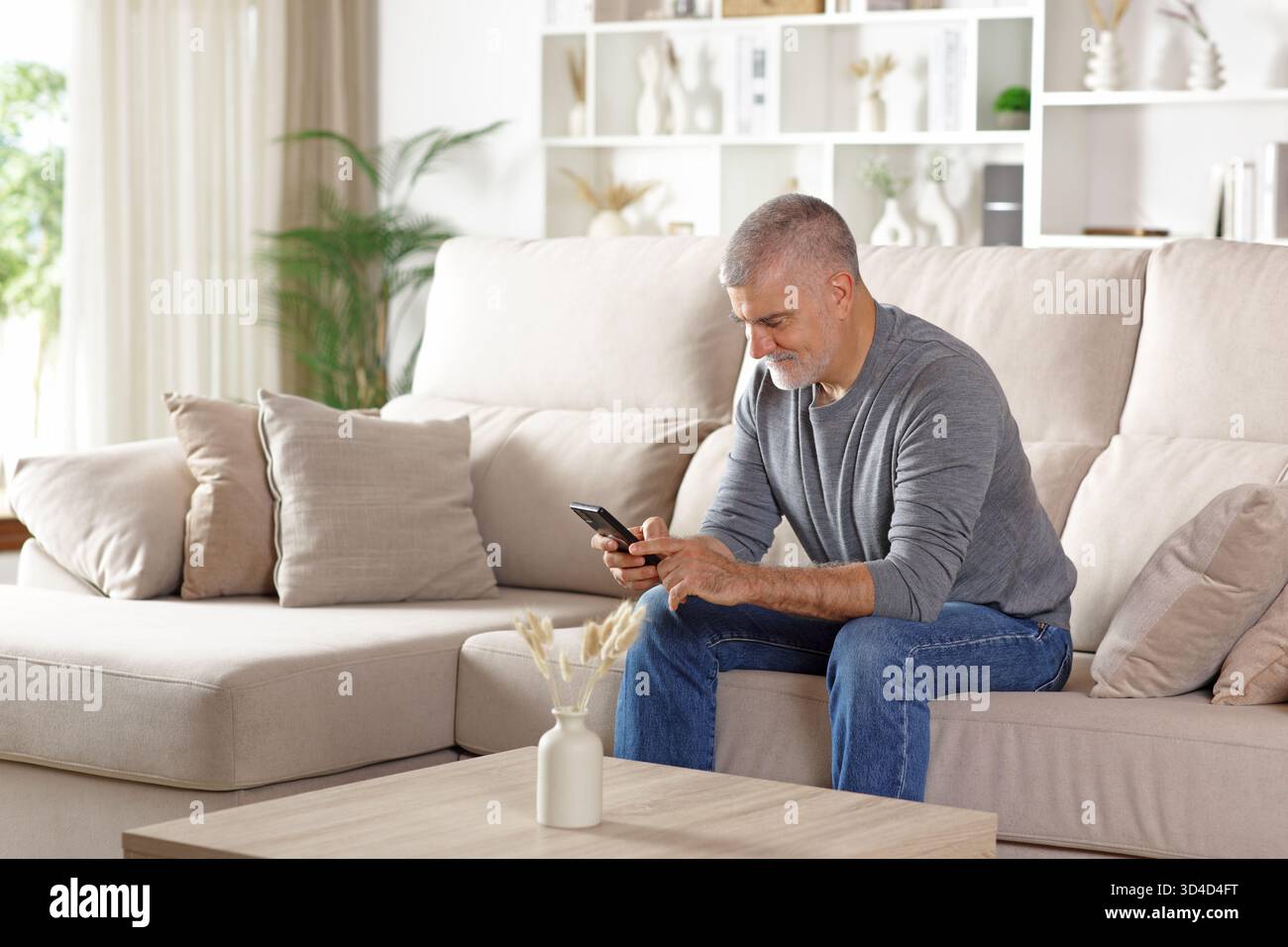 Happy senior man using cell phone sitting on a couch at home Stock Photo