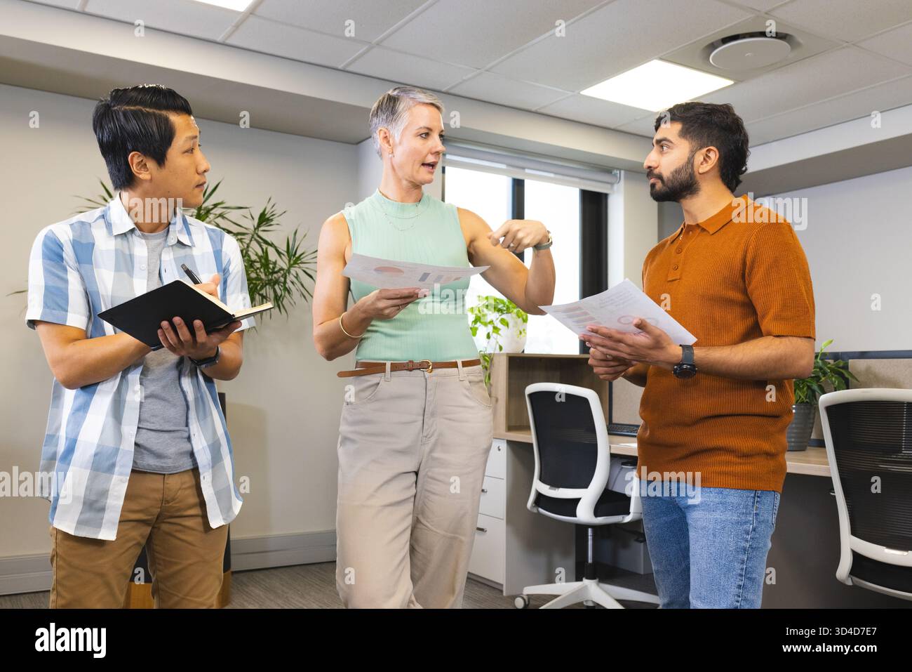 Diverse coworkers collaborating in open-plan office, using printed charts and notebooks Stock Photo