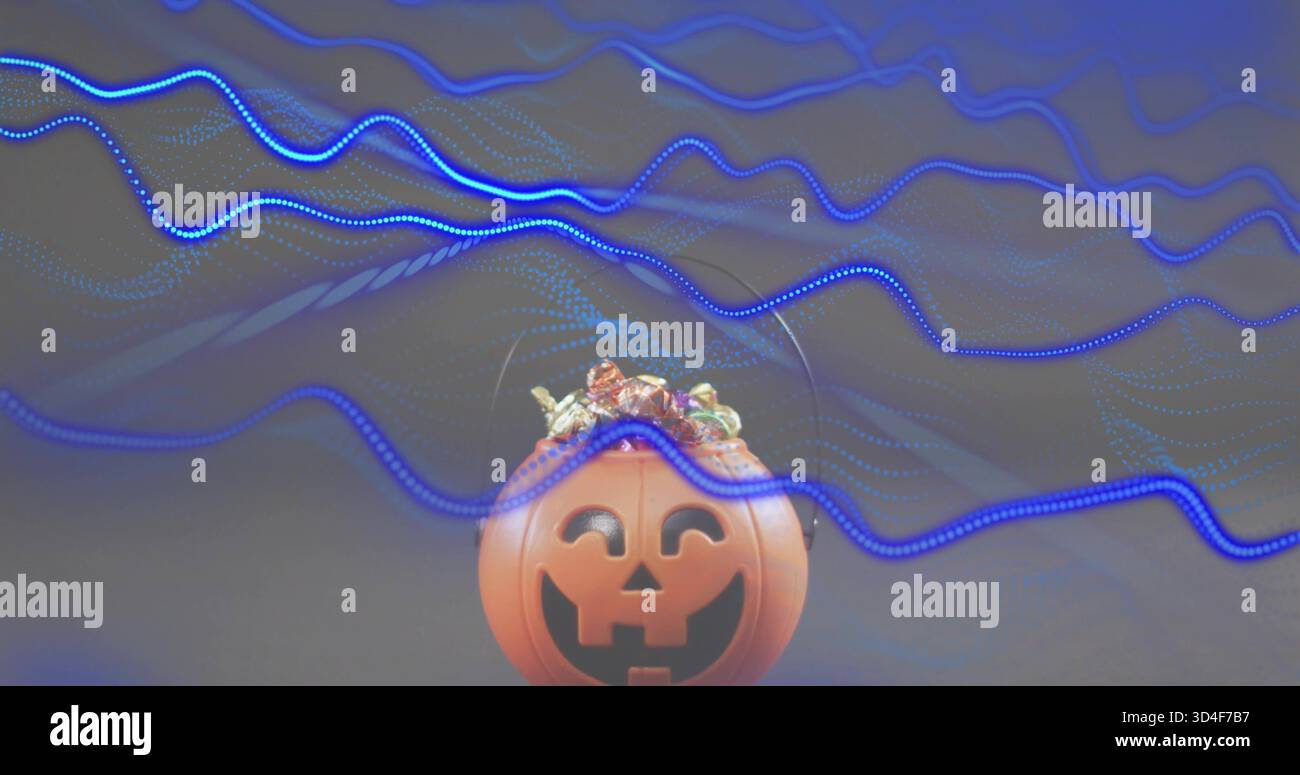Sitting orange plastic jack-o'-lantern bucket holding wrapped candies on studio table, blue streaks Stock Photo