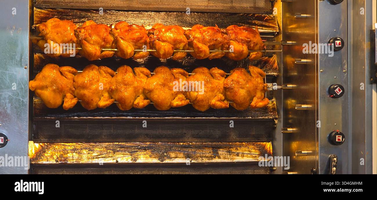 Rotisserie chicken is cooking on skewers inside a commercial kitchen appliance, showcasing golden-brown skin and delicious aroma. - Smartphone Captured Stock Image