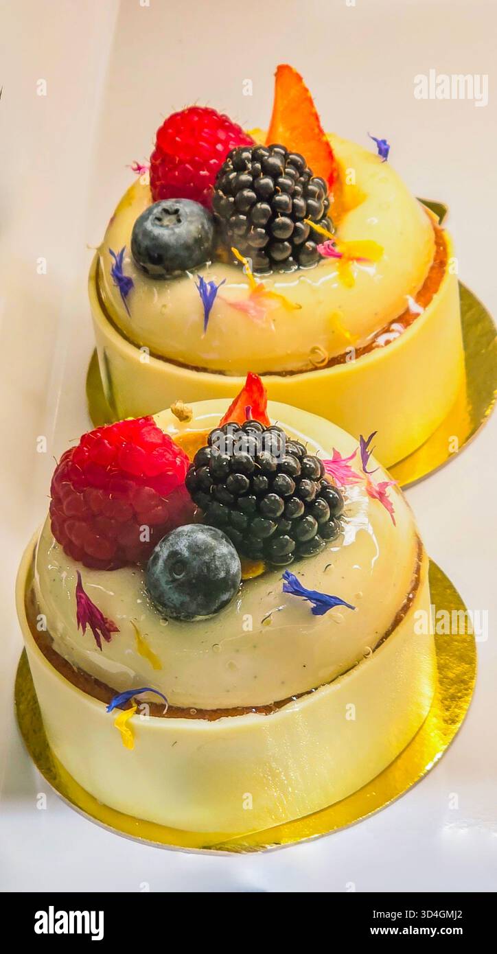 Elegant dessert cakes are beautifully adorned with fresh berries and vibrant edible flowers, showcasing a delightful culinary creation. - Smartphone Captured Stock Image