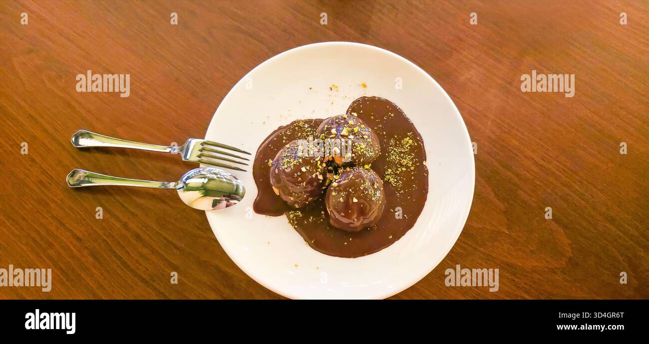 . Chocolate ice cream balls are elegantly drizzled with rich sauce on a white plate, creating a tempting dessert presentation - Smartphone Captured Stock Image