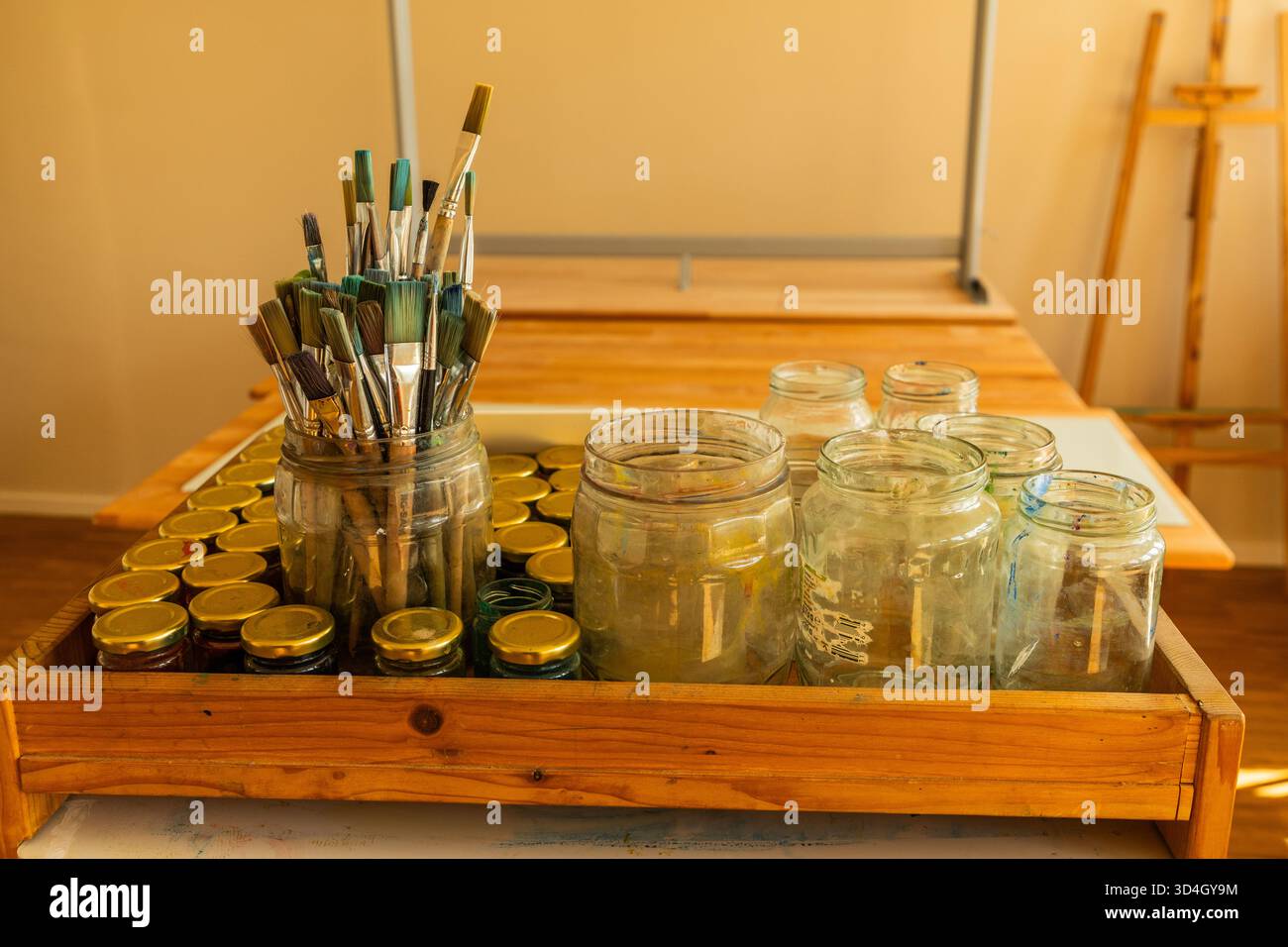 potbelly pig. Art supplies are neatly arranged on a wooden table, featuring jars filled with brushes and various containers for creative endeavors Stock Photo
