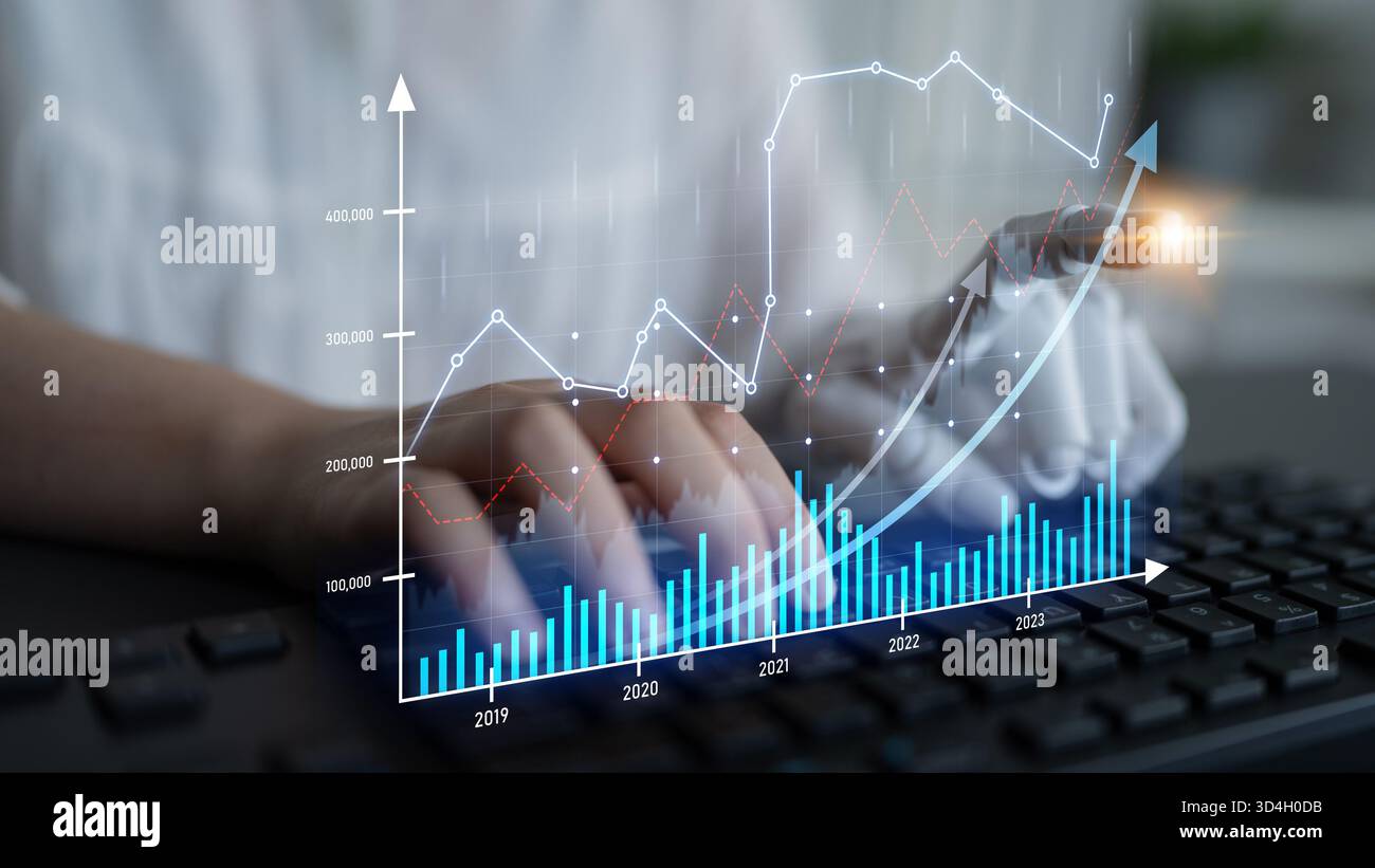 A focused data analyst interacts with financial graphs while typing on a keyboard, representing modern technology use in business analytics and Stock Photo
