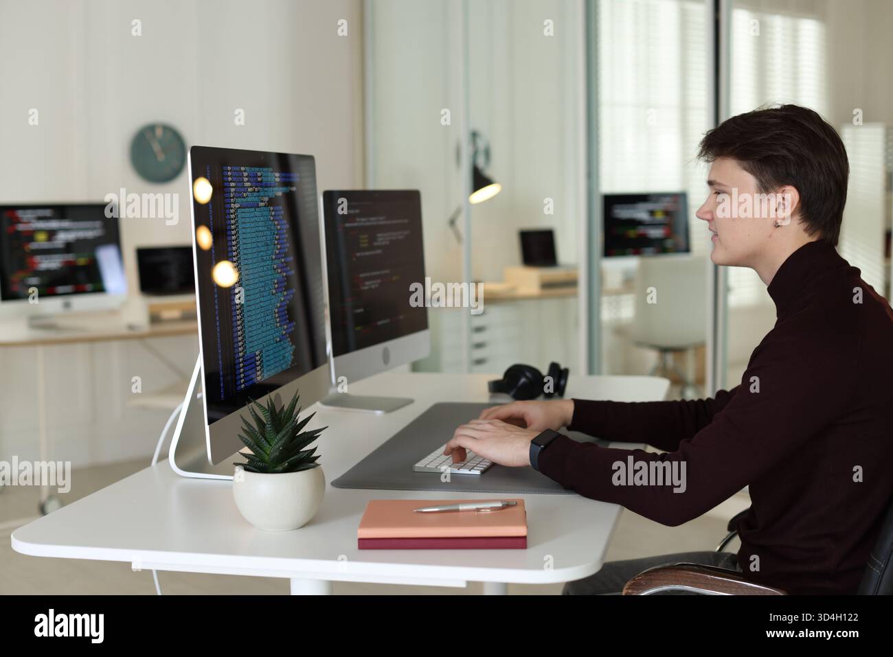 Programmer working on computer with dual monitors at white table in office Stock Photo