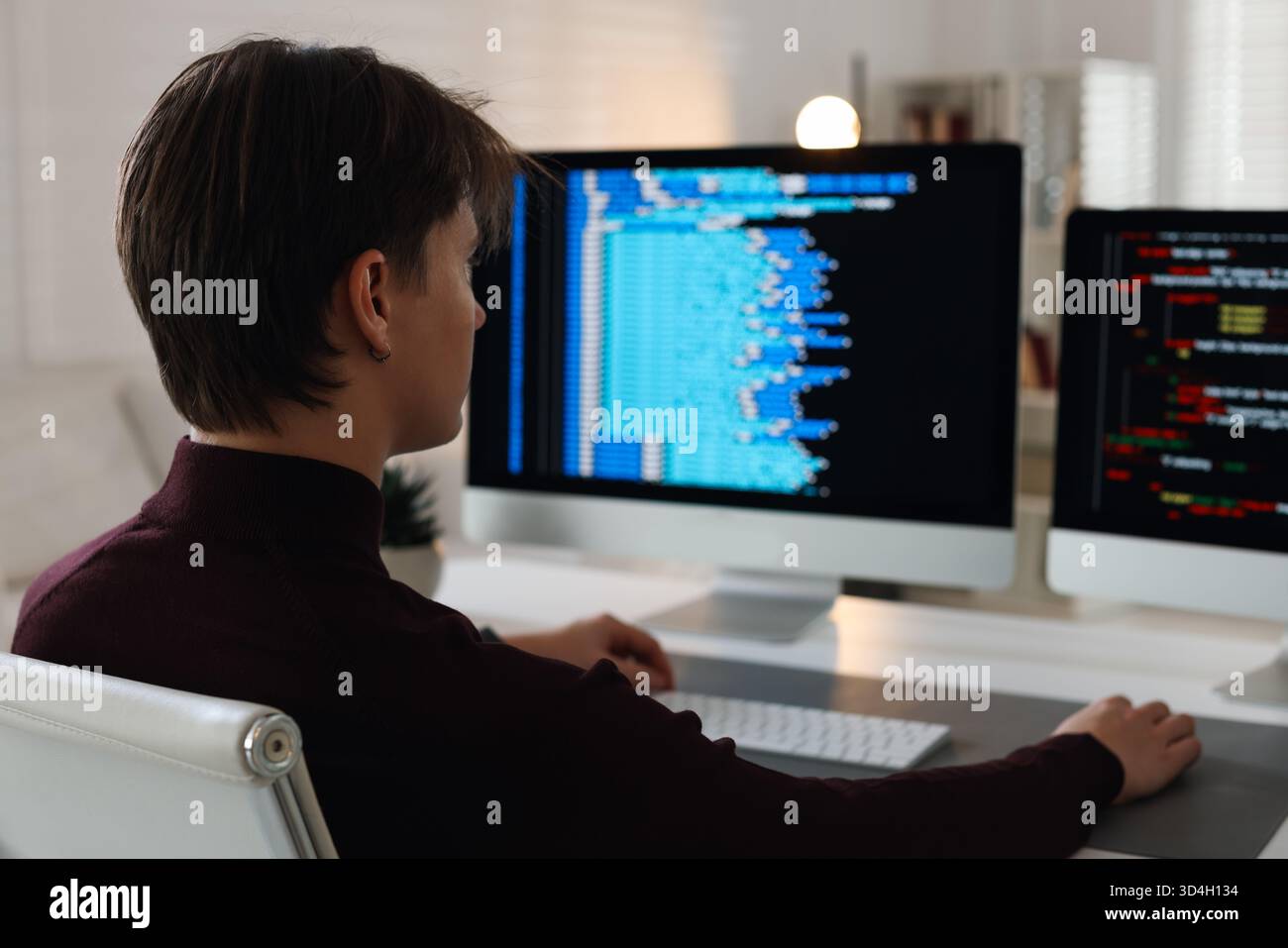 Programmer working on computer with dual monitors at white table in office Stock Photo