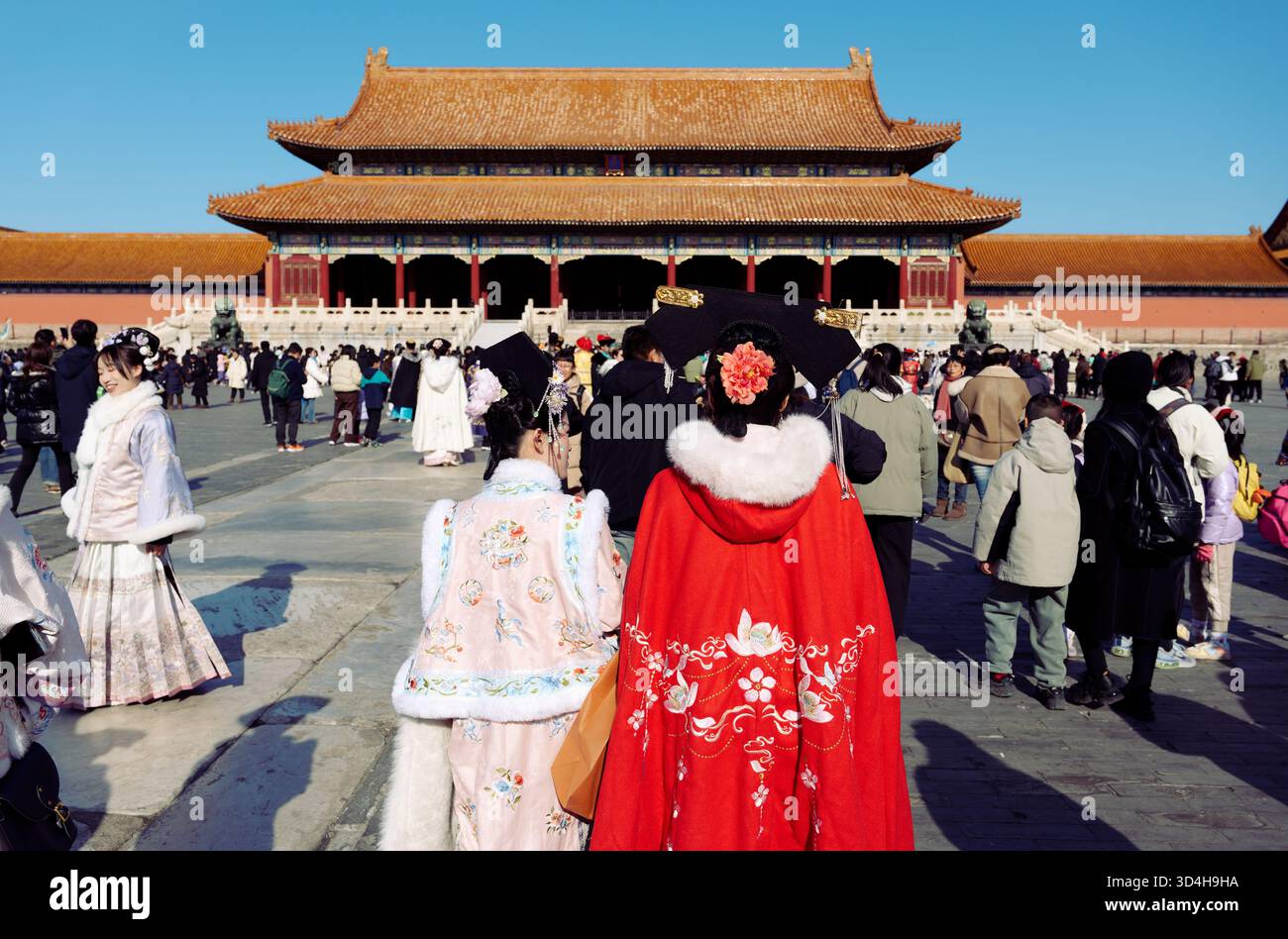 Inside the Forbidden City — visitors in colorful traditional attires cross the main courtyard toward a grand palace hall Stock Photo