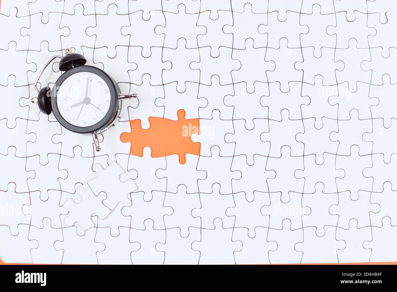 Alarm clock over missing puzzle piece suggests urgency, highlighting time's role in completing tasks or solving unresolved problems. Stock Photo