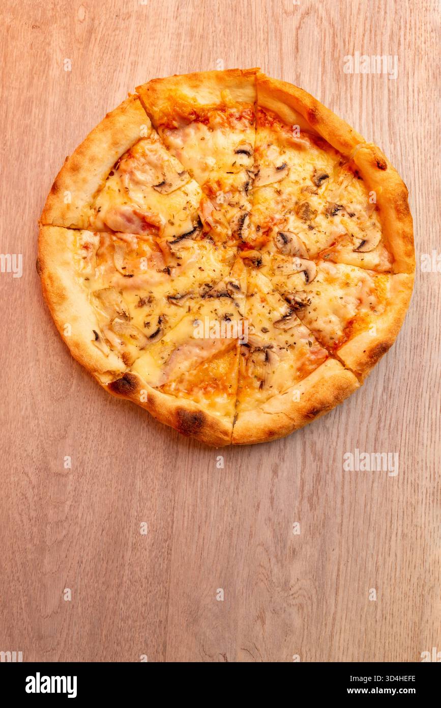 Top view of delicious pizza with melted cheese and mushrooms on wooden table, warm colors and crispy crust Stock Photo