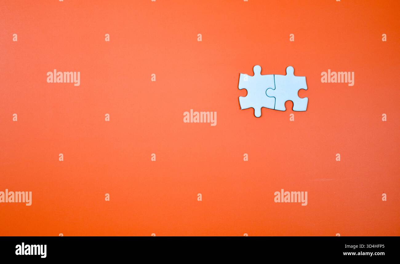 Two interlocked white puzzle pieces on orange background, symbolizing connection, unity, or problem-solving in a minimal visual composition. Stock Photo