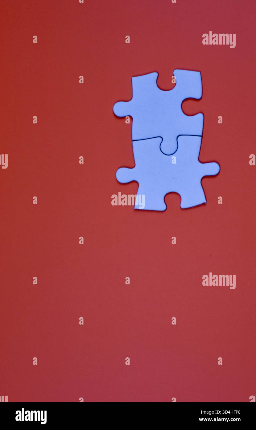 Two interlocked white puzzle pieces on orange background, symbolizing connection, unity, or problem-solving in a minimal visual composition. Stock Photo