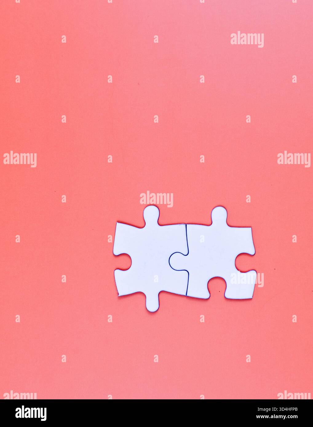 Two interlocked white puzzle pieces on orange background, symbolizing connection, unity, or problem-solving in a minimal visual composition. Stock Photo