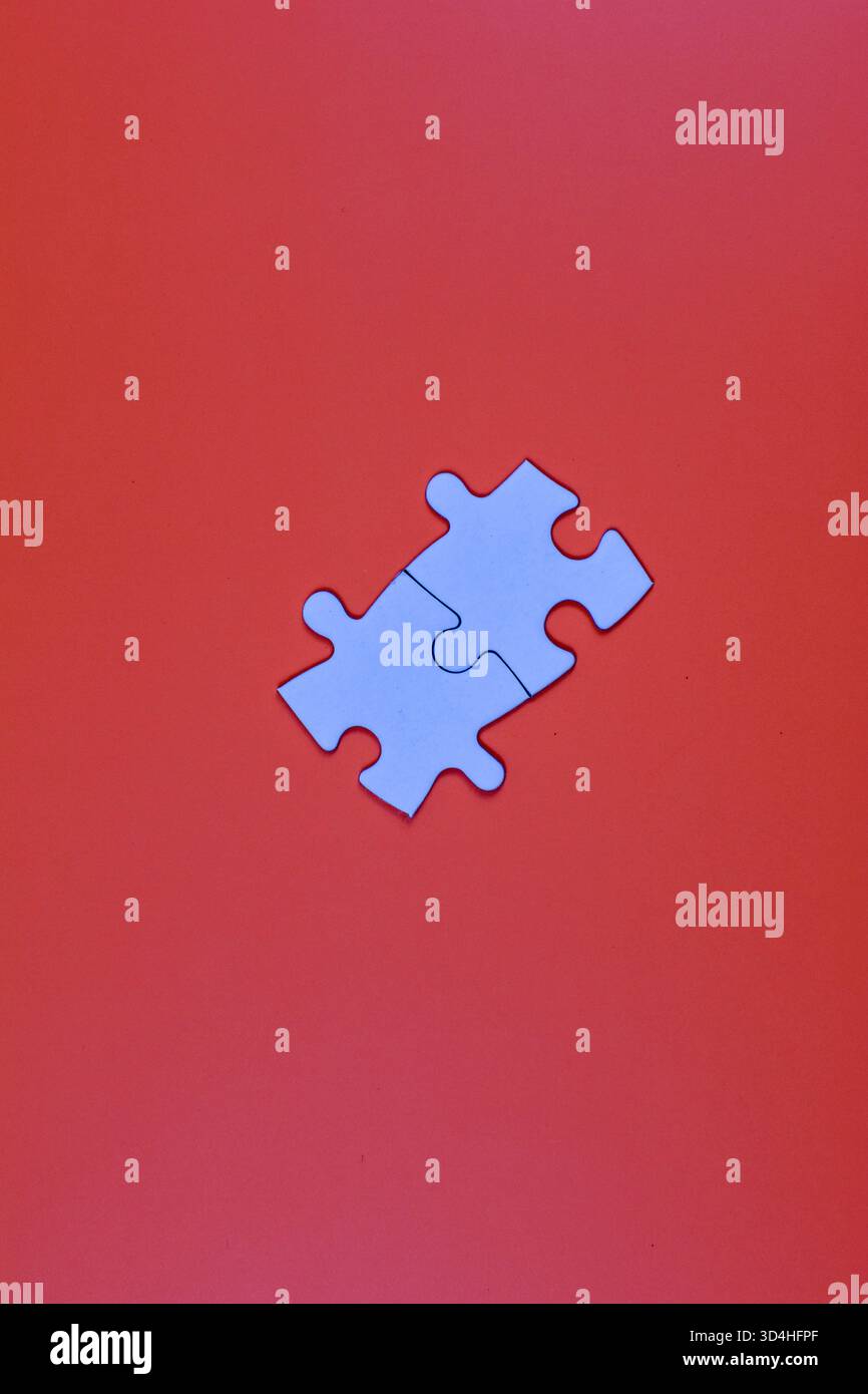 Two interlocked white puzzle pieces on orange background, symbolizing connection, unity, or problem-solving in a minimal visual composition. Stock Photo