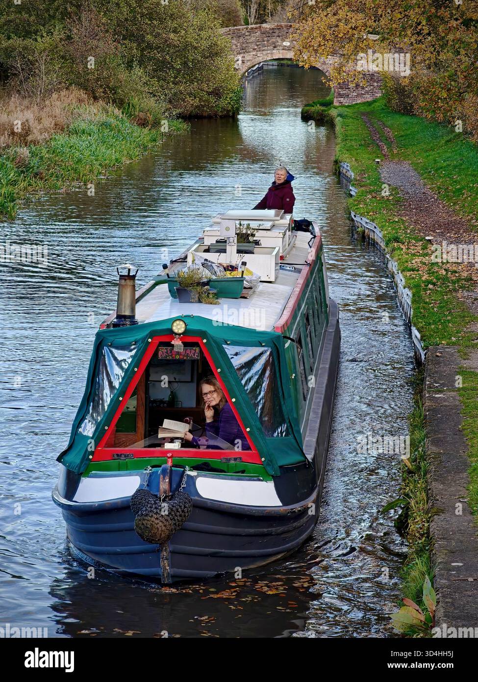 A narrowboat cruising along the Llangollen Canal near Wrenbury in rural Shropshire, England, United Kingdom, in November 2025. with a woman steering - Smartphone Captured Stock Image