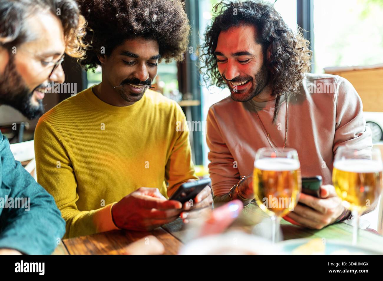 Friends drinking beer and using smartphone in bar Stock Photo