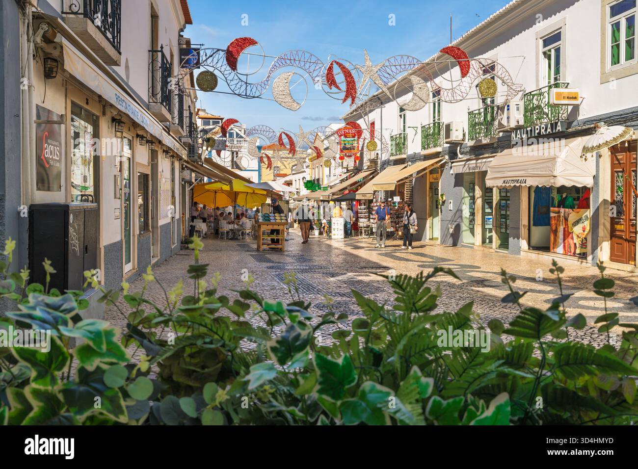 Lagos, Portugal, November 8, 2025. Festive lights and yellow umbrellas create a lively and welcoming atmosphere along a pedestrian shopping street fil Stock Photo