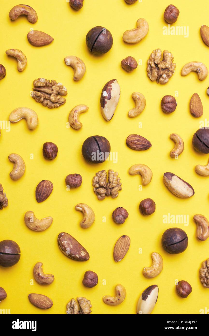 Pattern of nuts mix. Hazelnut, macadamia, almonds, walnut, cashew, brazil nut, on yellow background. Top view. Stock Photo