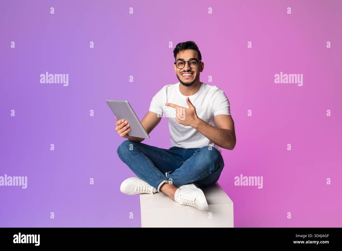 Handsome Millennial Arab Man Engages With Digital Tablet in Neon Light Setting While Sitting Stock Photo
