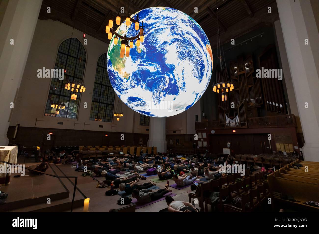 Seattle, Washington, USA. 10th November 2025. People practice yoga under a monumental globe in the nave of Saint Mark's Episcopal Cathedral. The TERRA Exhibition, a 24 foot diameter globe created by Eric Morris of Orbis World Globes, features NASA’s Blue Marble satellite imagery. Credit: Paul Christian Gordon/Alamy Live News Stock Photo