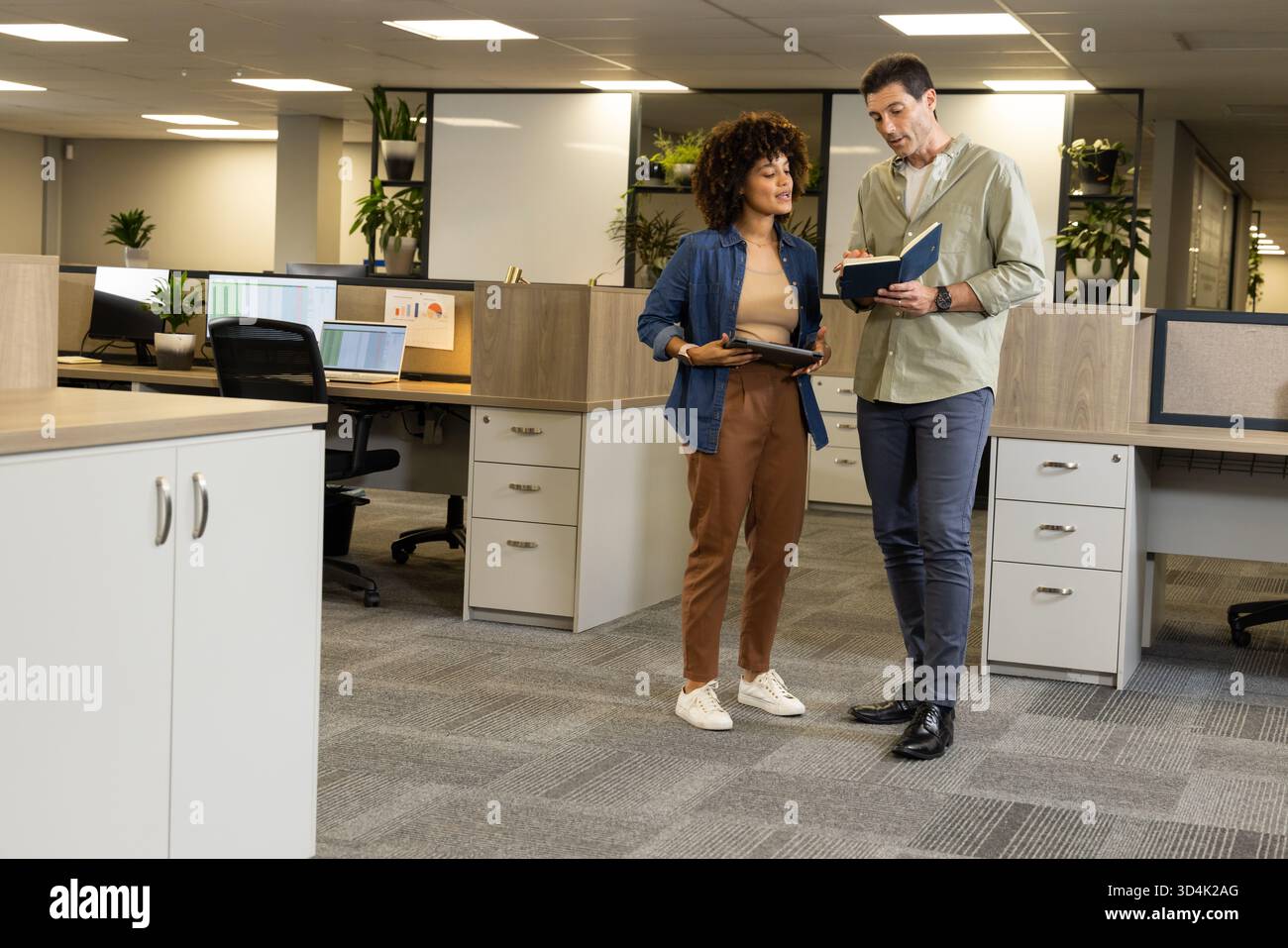 Discussing Diverse coworkers reviewing project plans in open-plan office, with tablet and notebook Stock Photo
