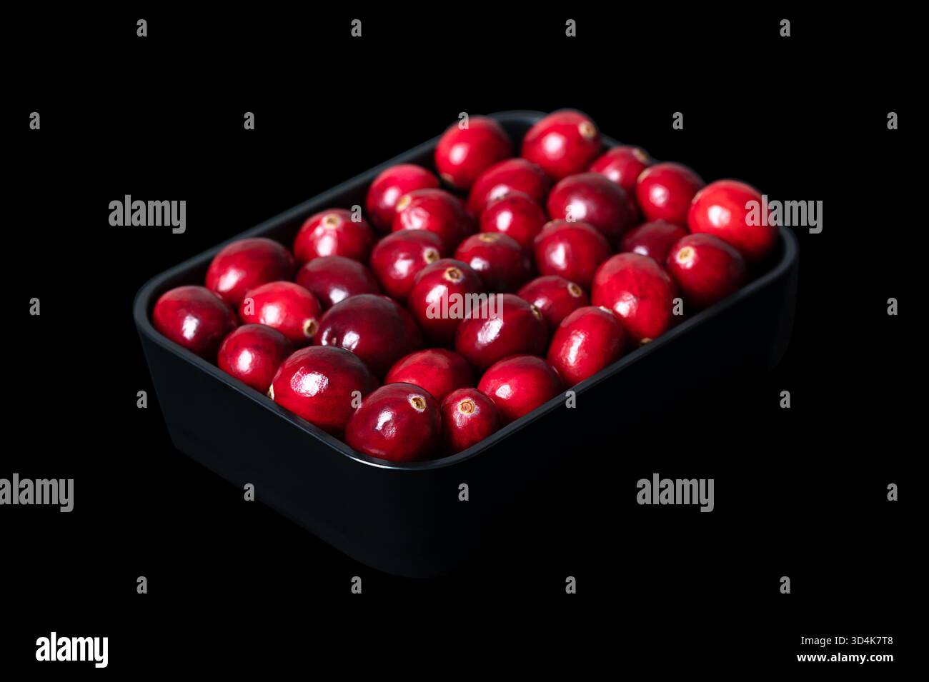Fresh large cranberries, in a black bowl, isolated on black background. Oblique view on bearberries, ripe and bright red American cranberries. Stock Photo
