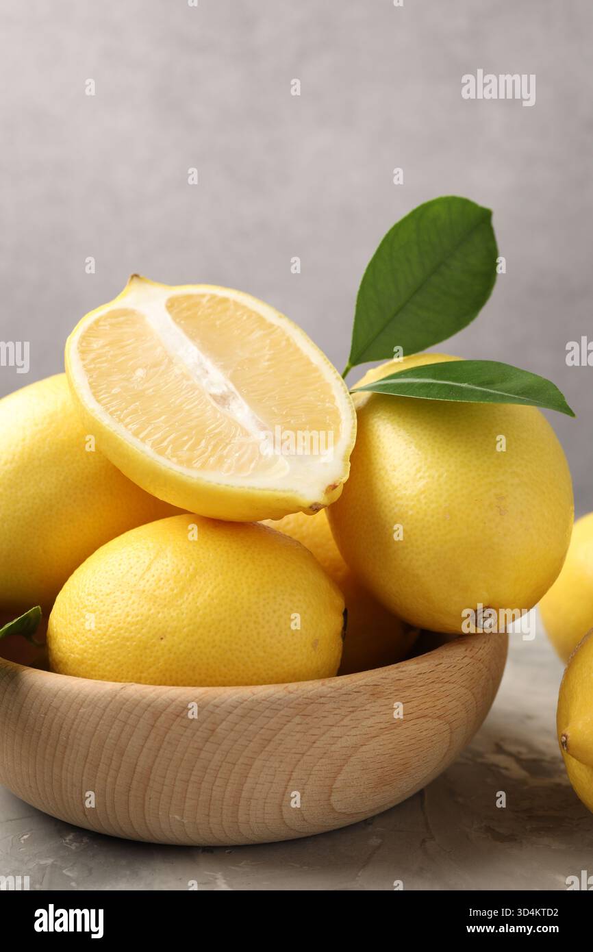 Whole, cut lemons with green leaves and bowl on grey textured table ...