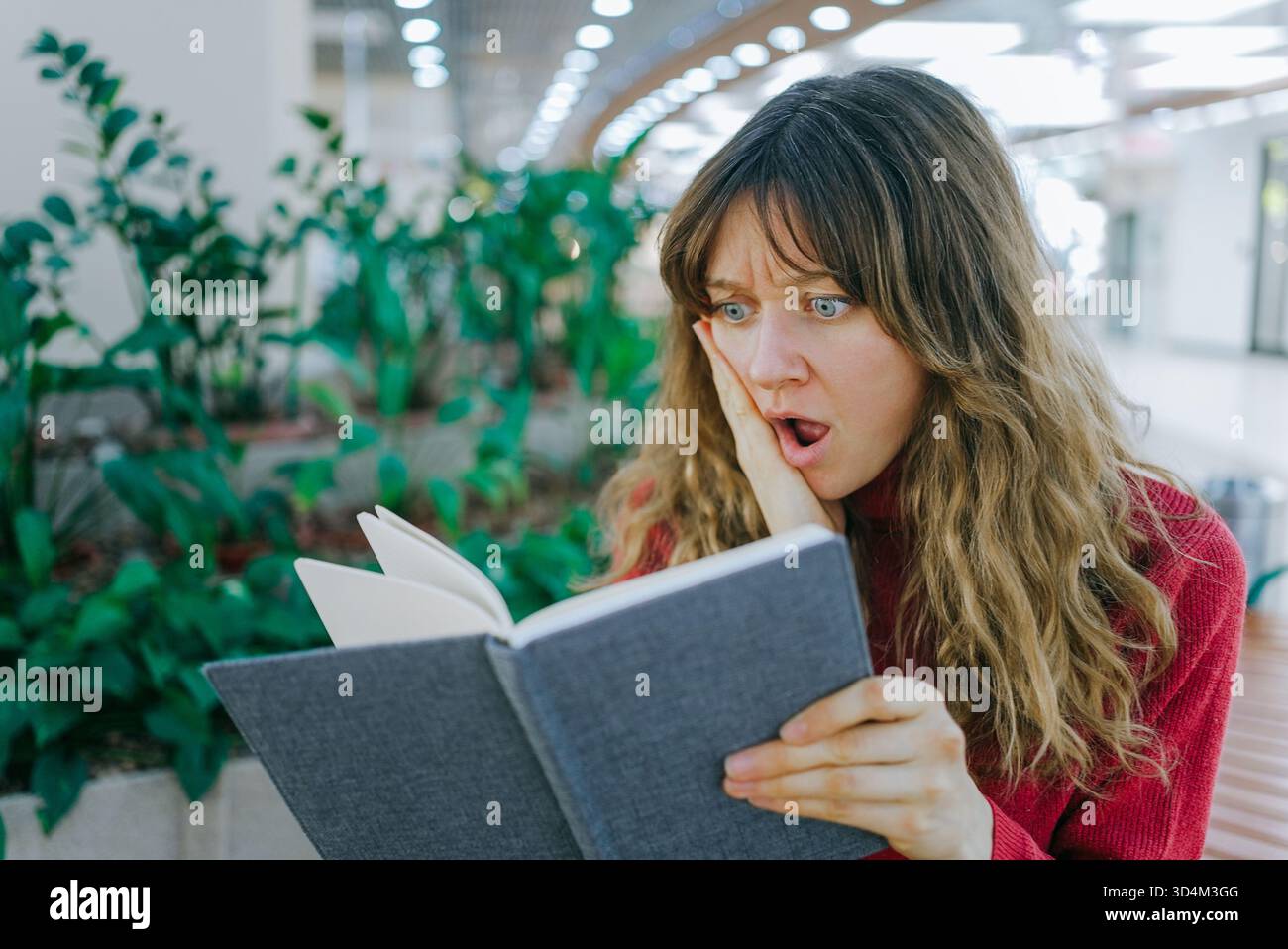 Woman reading a book, reacting with an open mouth and wide eyes ...