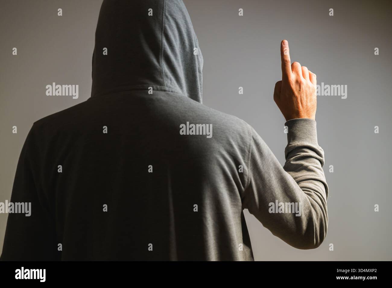 Rear view of man in hoodie raising index finger as if pointing or clicking on invisible virtual screen, tech concept. Selective focus. Stock Photo