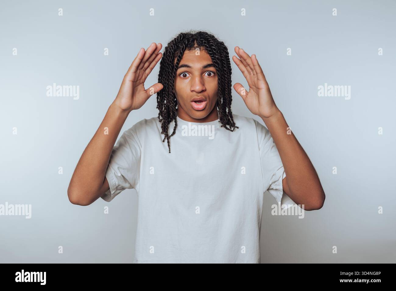 A young man with curly hair stands in a studio, expressing surprise. Stock Photo