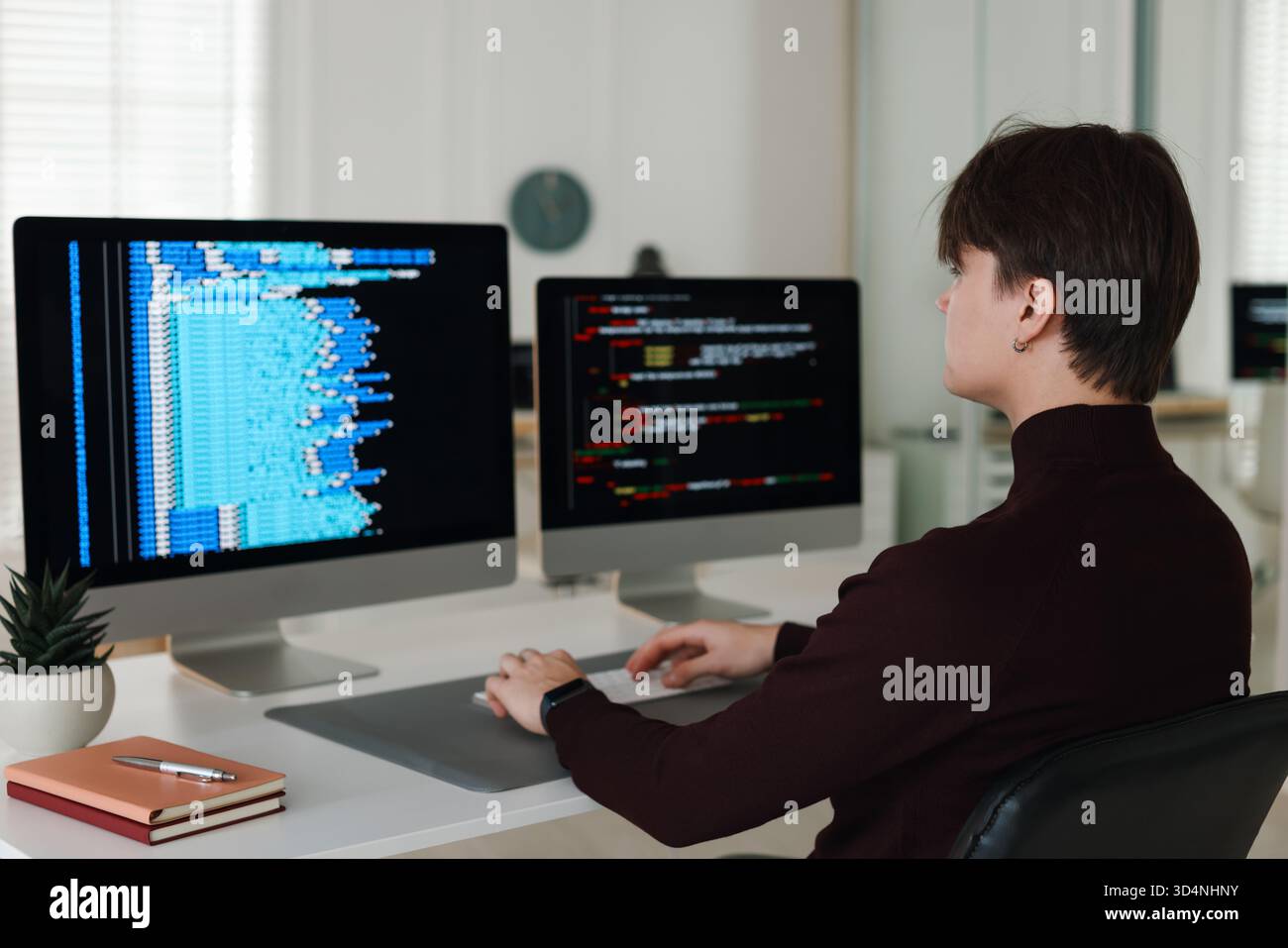 Programmer working on computer with dual monitors at white table in office Stock Photo