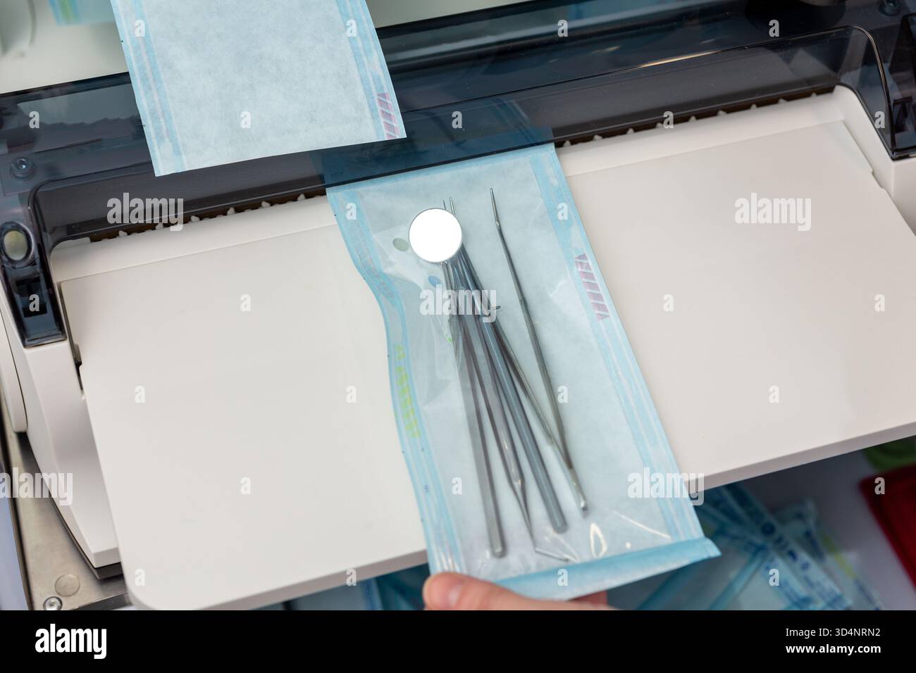 A medical professional uses a constant heat sealing machine to prepare a sterilization pouch containing dental instruments (mirror, explorer, probe) f Stock Photo