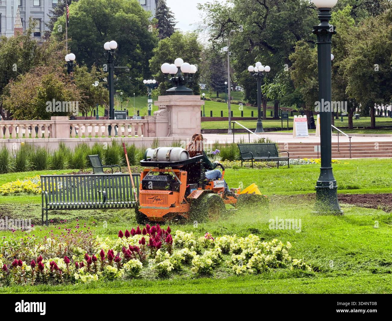 Denver, Colorado, USA - 2 June 2025: Person driving a ride on lawn mower to cut grass in a city park - Smartphone Captured Stock Image