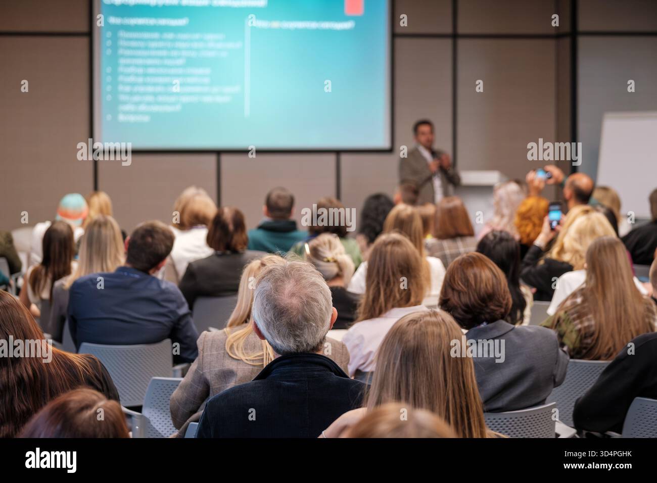 Engaged audience at business conference listening to speaker in modern lecture hall with projector screen Stock Photo