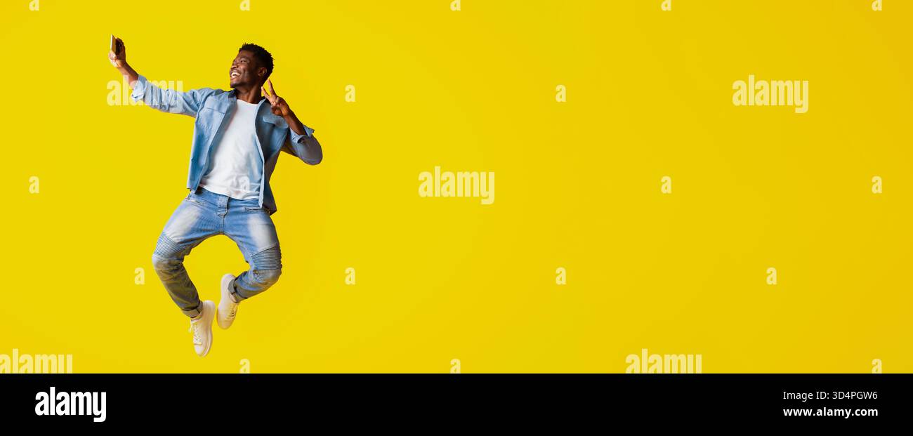 Man Jumping Joyfully While Taking a Selfie on a Bright Yellow Background Stock Photo