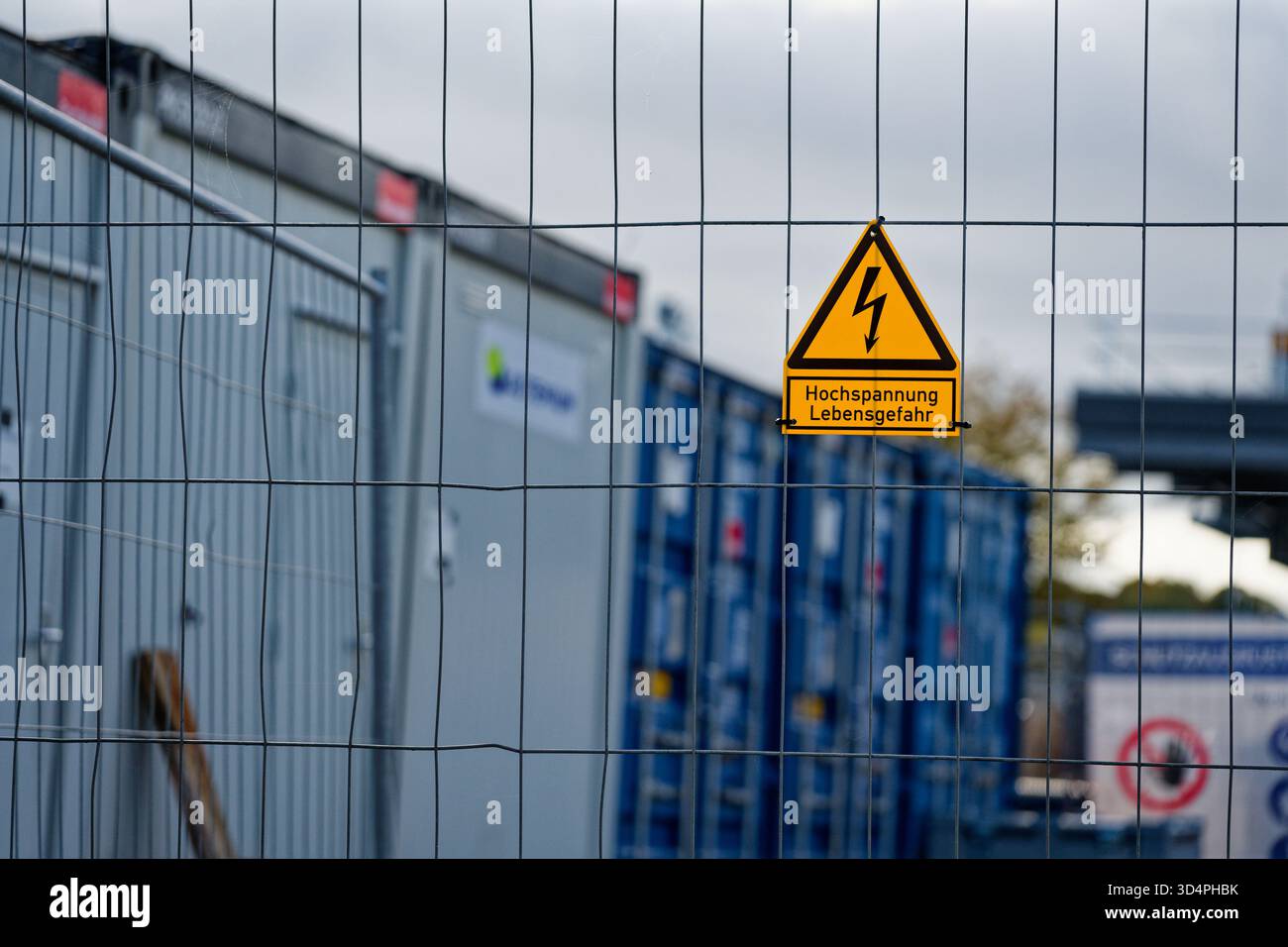 A wire mesh fence holds a bright yellow triangle sign with a black ...