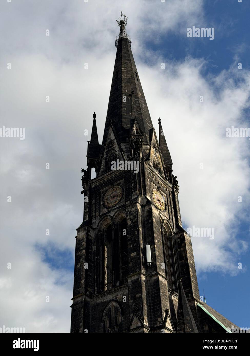 Historic Gothic church clock tower with a tall spire rising into a partly cloudy sky. - Smartphone Captured Stock Image
