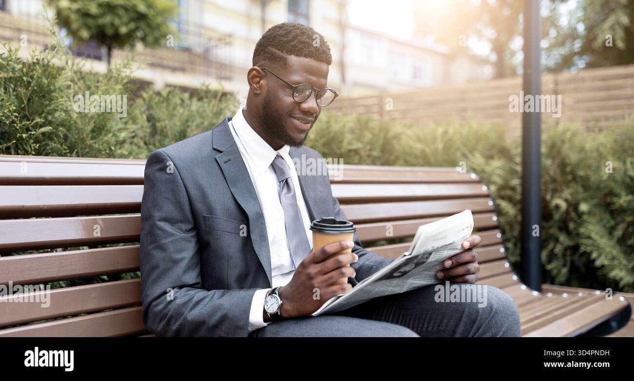 Young Man in a Suit Enjoys Coffee and Reads Newspaper in Park During Daytime Stock Photo