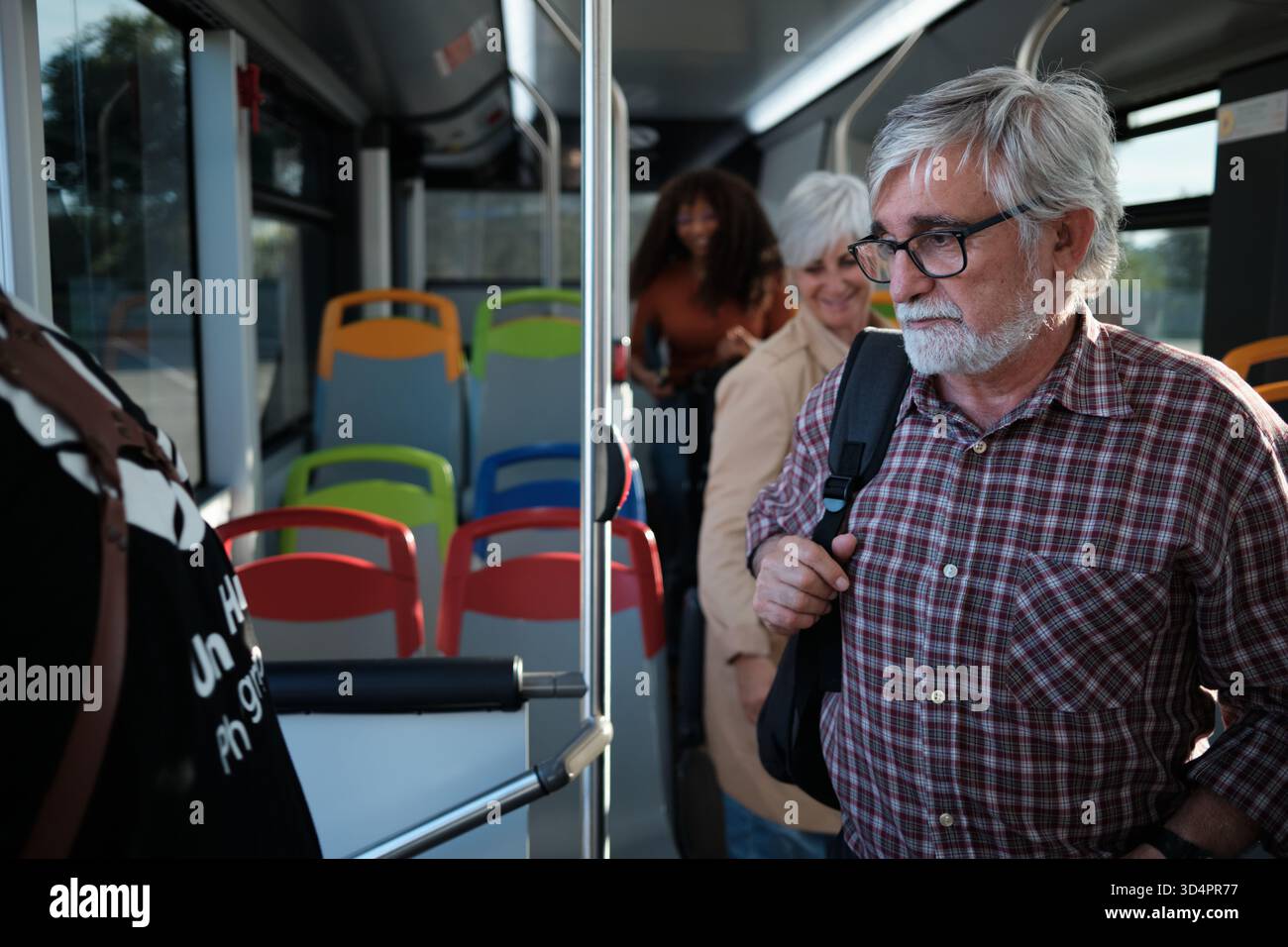 Senior man commuting on bus, standing with backpack Stock Photo