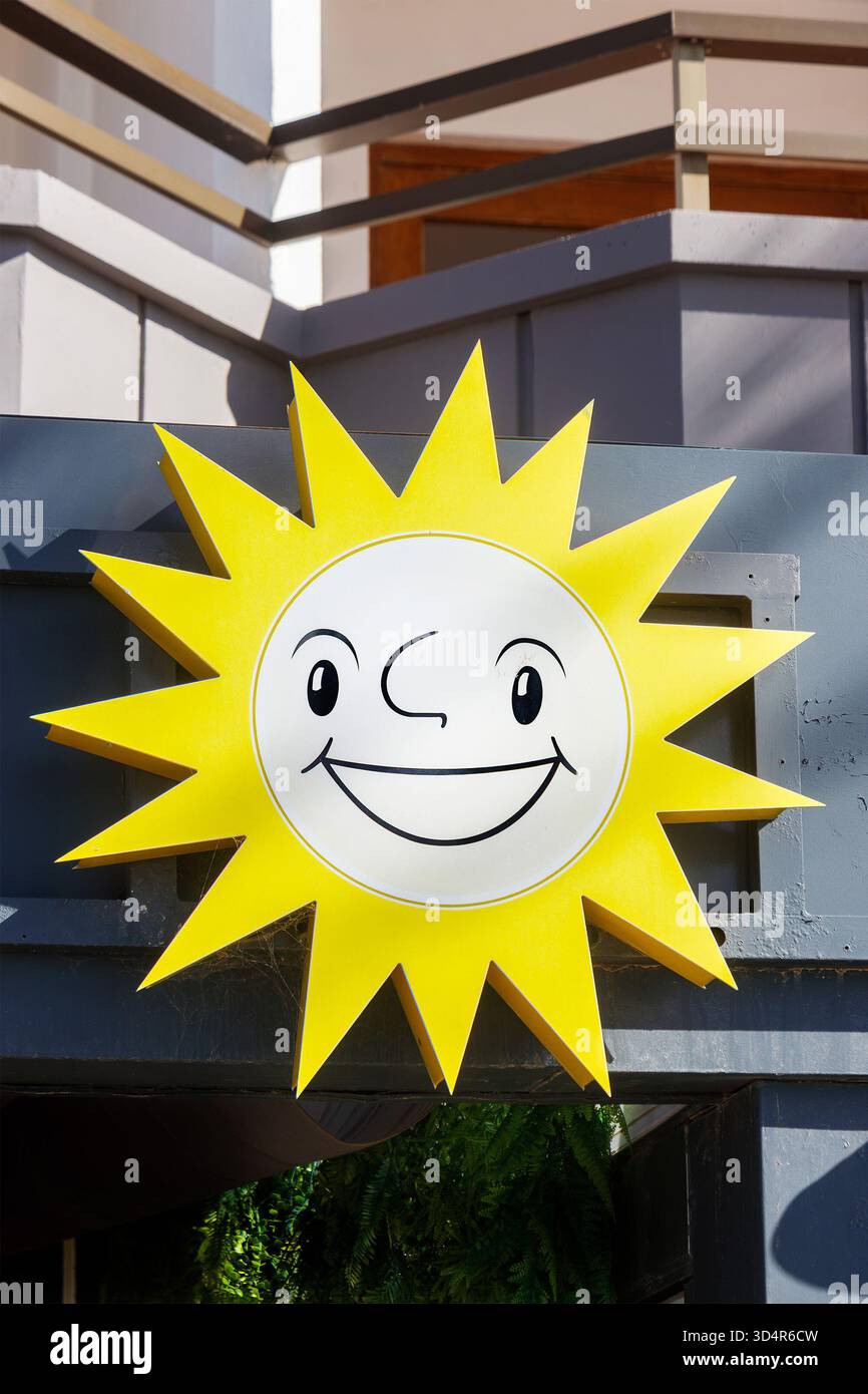Bright yellow smiling sun cartoon sign with a cartoon face mounted on a building exterior under natural light Stock Photo