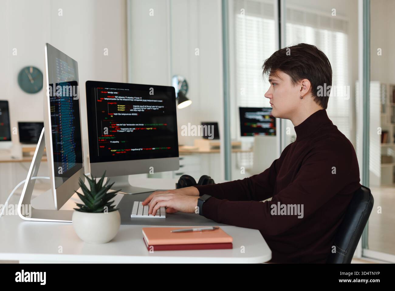 Programmer working on computer with dual monitors at white table in office Stock Photo