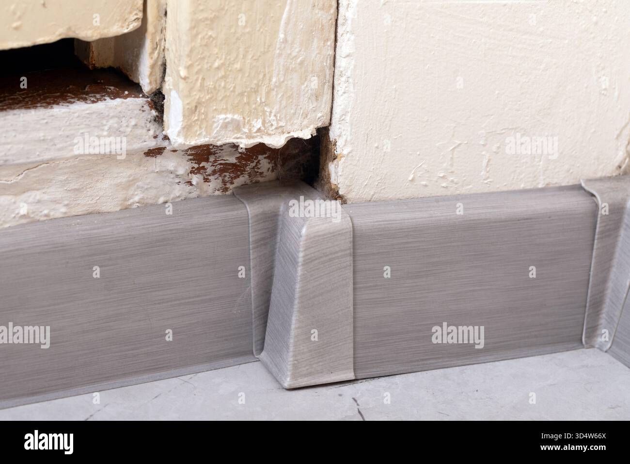 Close-up of a chipped wall corner with metal baseboard molding. Neutral colors highlight texture, ideal for renovation, construction, or interior desi Stock Photo