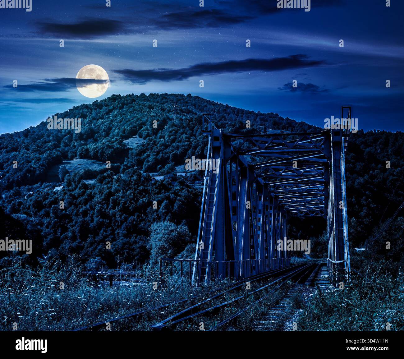 old metal rail road bridge in rural area in mountains at night. journey through beautiful landscape in full moon light. transportation or technology b Stock Photo
