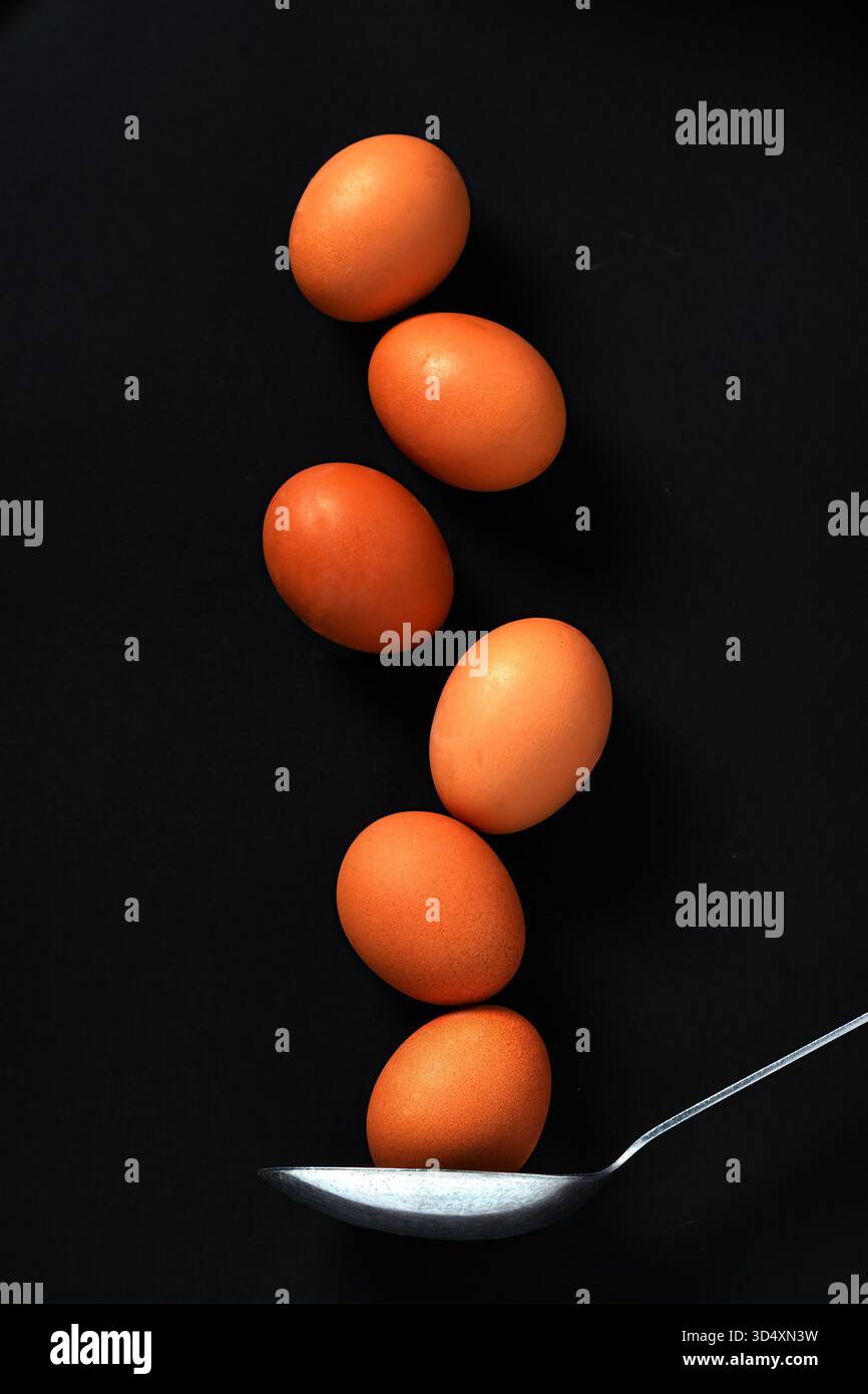 six brown eggs in a vertical  column with large spoon underneath Stock Photo