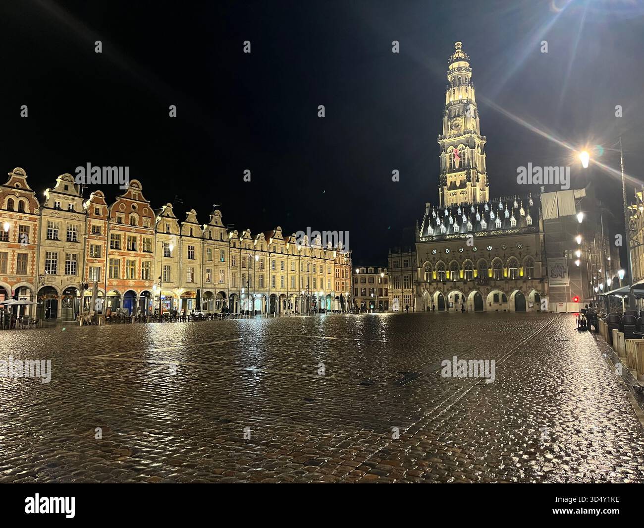 Grand Place in Arras, France, at night with the illuminated town hall and belfry reflected on the wet cobblestones - Smartphone Captured Stock Image