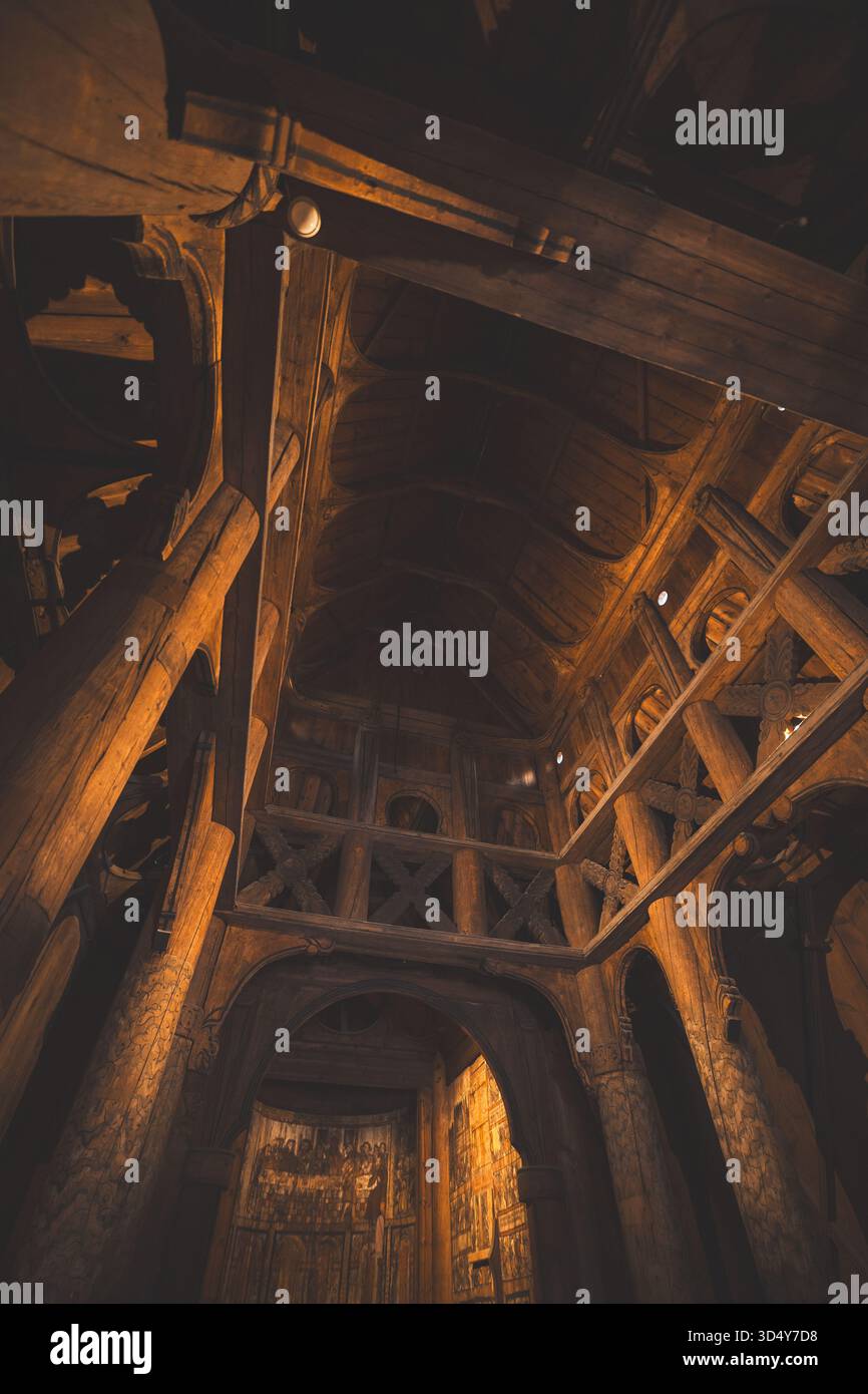 Warm light reveals the intricate wooden interior of Gol Stave Church in Oslo, Norway, carved pillars, arches, and medieval Christian artistry. Stock Photo