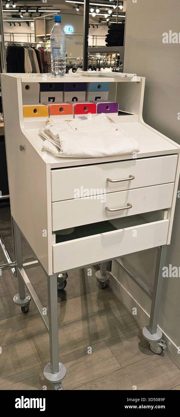 Berlin, Germany - September 22, 2025: White display cart features colorful fabric swatches and folded clothes in retail environment. - Smartphone Captured Stock Image