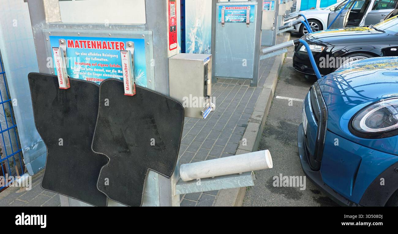 Berlin, Germany - September 27, 2025: Car wash area features black mats hanging with blue vehicle parked nearby. - Smartphone Captured Stock Image