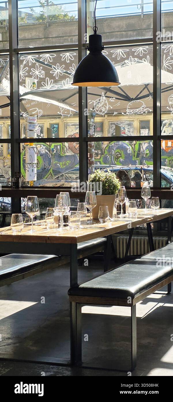 Berlin, Germany - September 28, 2025: . Modern dining area features wooden table with glassware and greenery decor - Smartphone Captured Stock Image