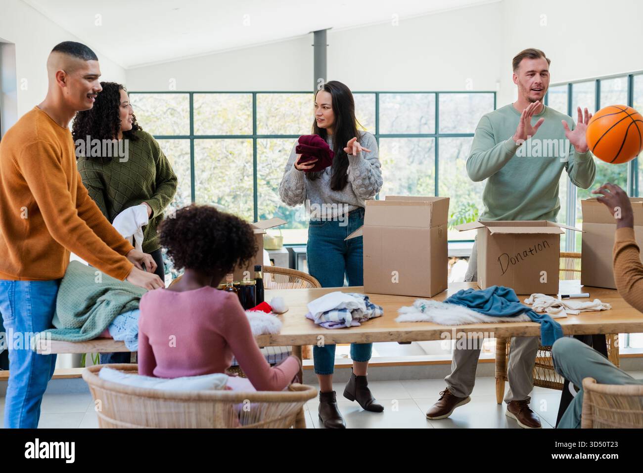 Diverse volunteers sorting and folding clothes at table in community center with donation boxes Stock Photo